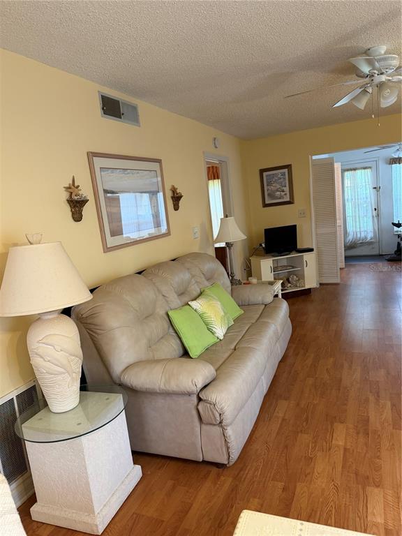 A living room features a beige sofa, a dolphin-base lamp, and wood-look flooring — 2400 WINDING CREEK BOULEVARD UNIT 18A-110, CLEARWATER, FL