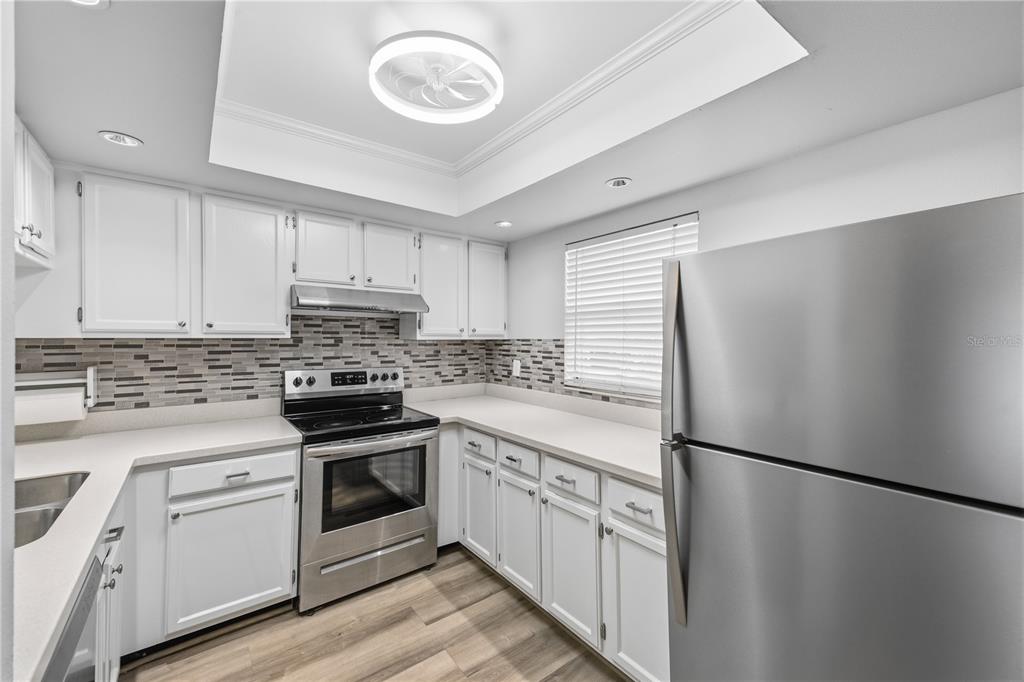 A kitchen with white cabinets, stainless steel appliances, a tiled backsplash, and wood-look flooring — 5108 LAWNTON COURT, TAMPA, FL