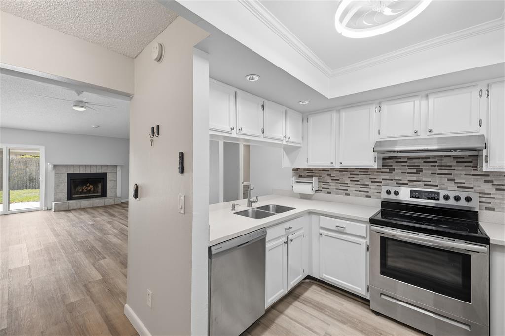 A kitchen with white cabinets, stainless steel appliances, and a tiled backsplash overlooks a living area — 5108 LAWNTON COURT, TAMPA, FL