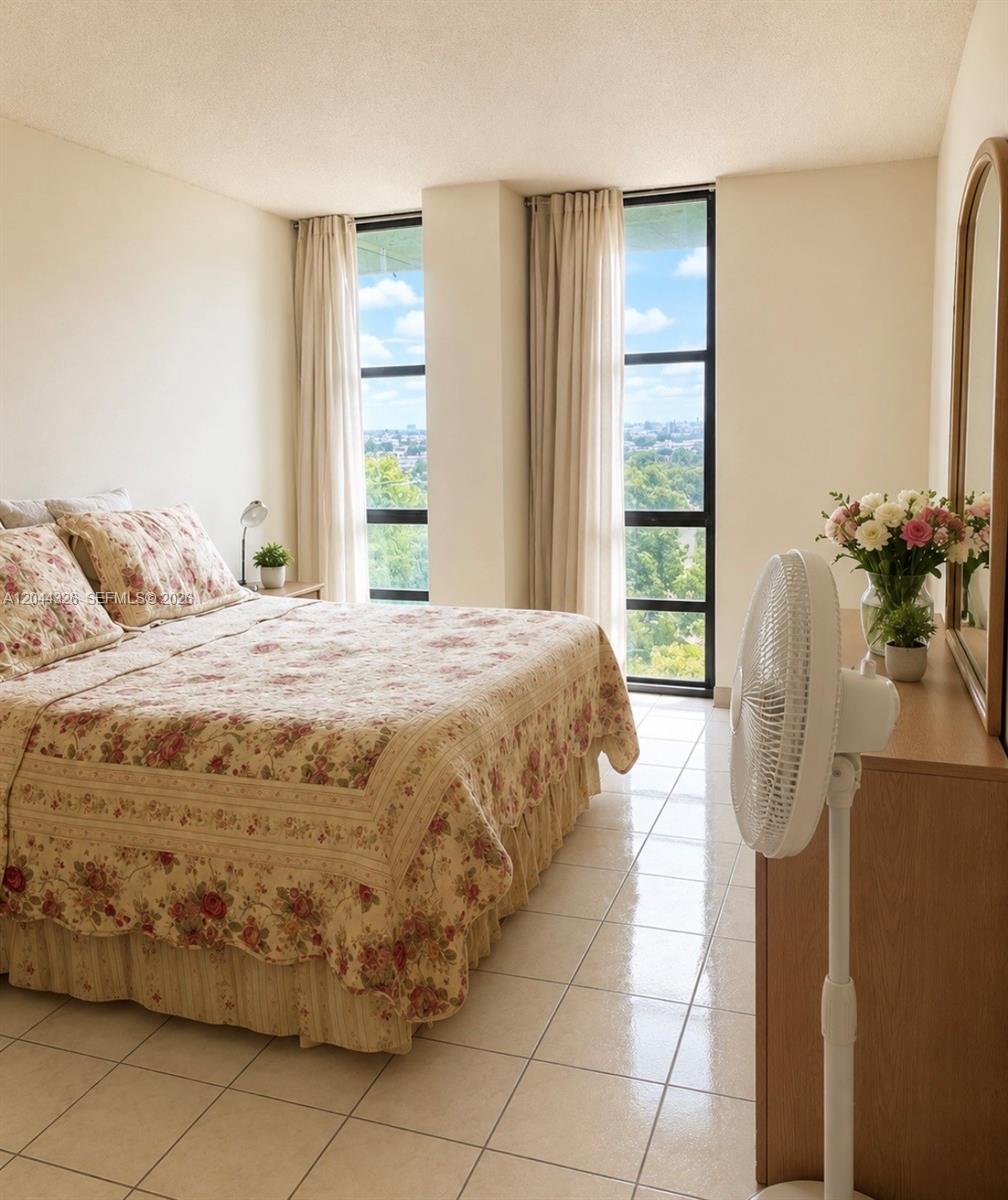 A bedroom with a floral bedspread, tile flooring, and two tall windows overlooking a city — 1825 W 44th Pl # 806, Hialeah FL 33012, HIALEAH, FL
