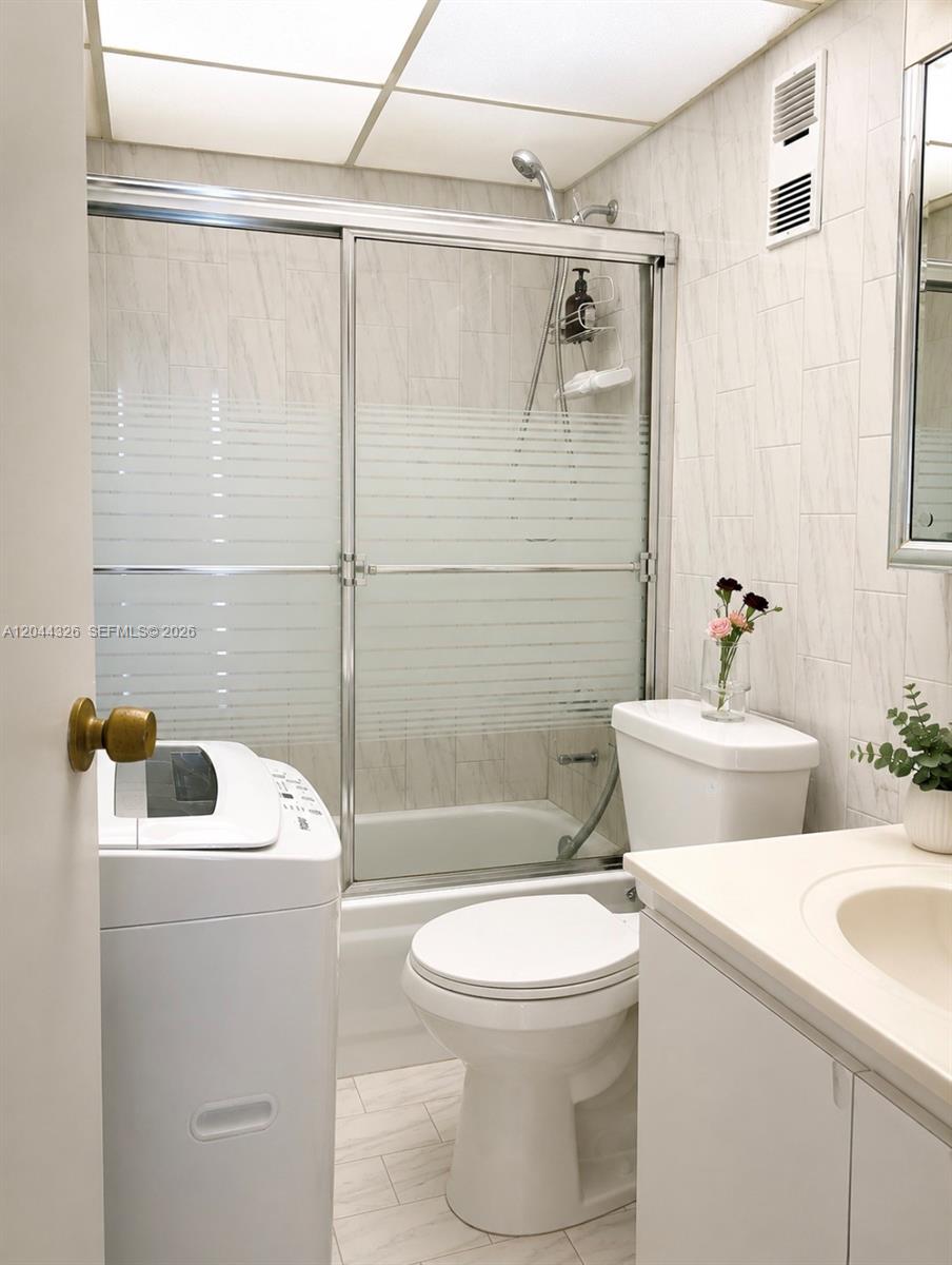 A bathroom features a white vanity, toilet, shower-tub combination, and a portable washing machine — 1825 W 44th Pl # 806, Hialeah FL 33012, HIALEAH, FL