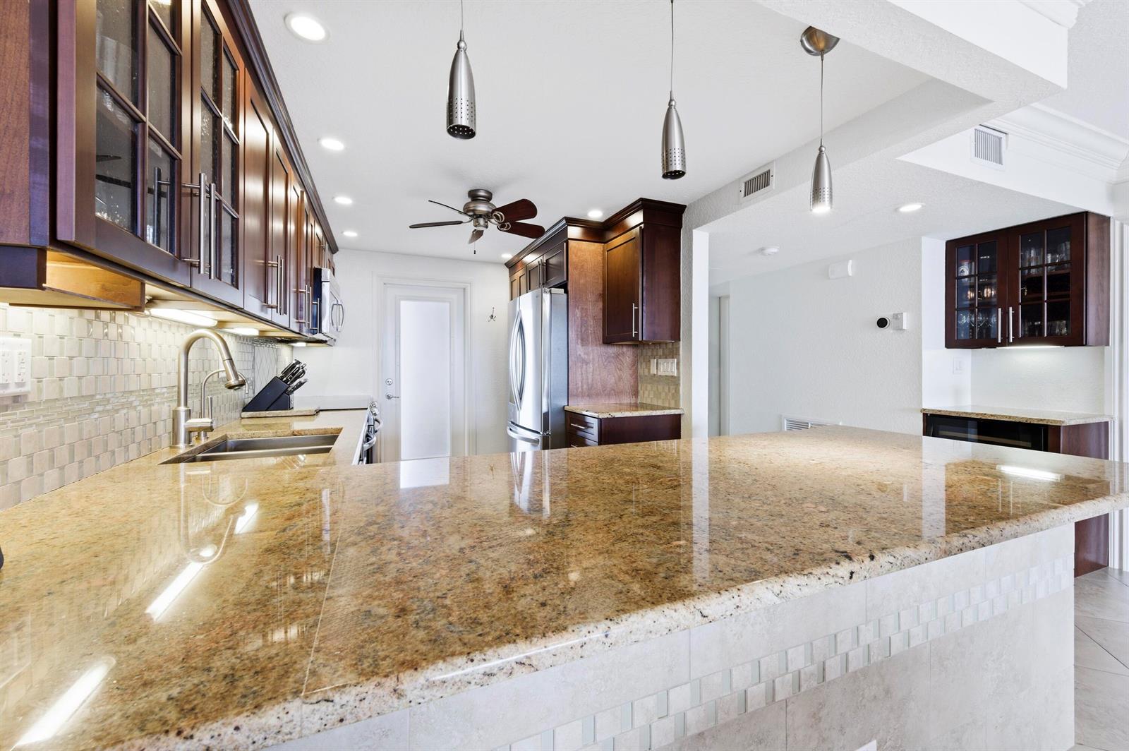 A kitchen features dark wood cabinets, granite countertops, stainless steel appliances, and three pendant lights — 3000 NE 48th Court # 406, Lighthouse Point FL 33064, LIGHTHOUSE POINT, FL