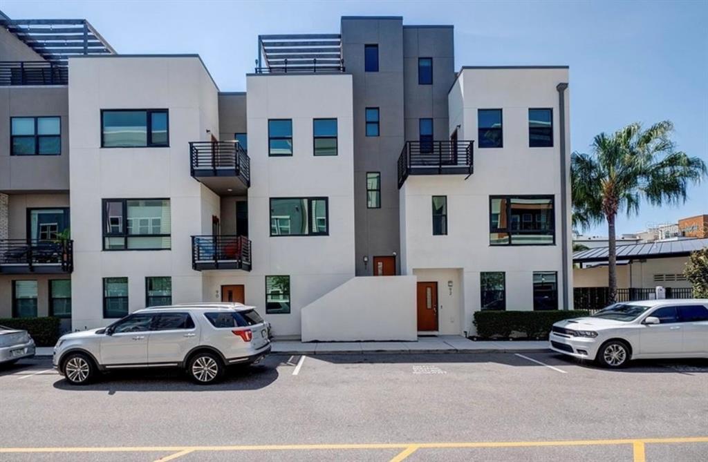 A modern three-story townhouse exterior with white and gray siding, balconies, and parked cars — 2511 N GRADY AVENUE UNIT 91, TAMPA, FL
