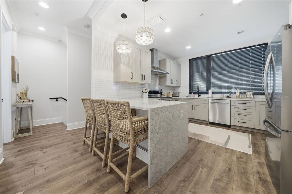 A modern kitchen features a stone-topped island with three woven bar stools and light cabinetry — 2511 N GRADY AVENUE UNIT 91, TAMPA, FL