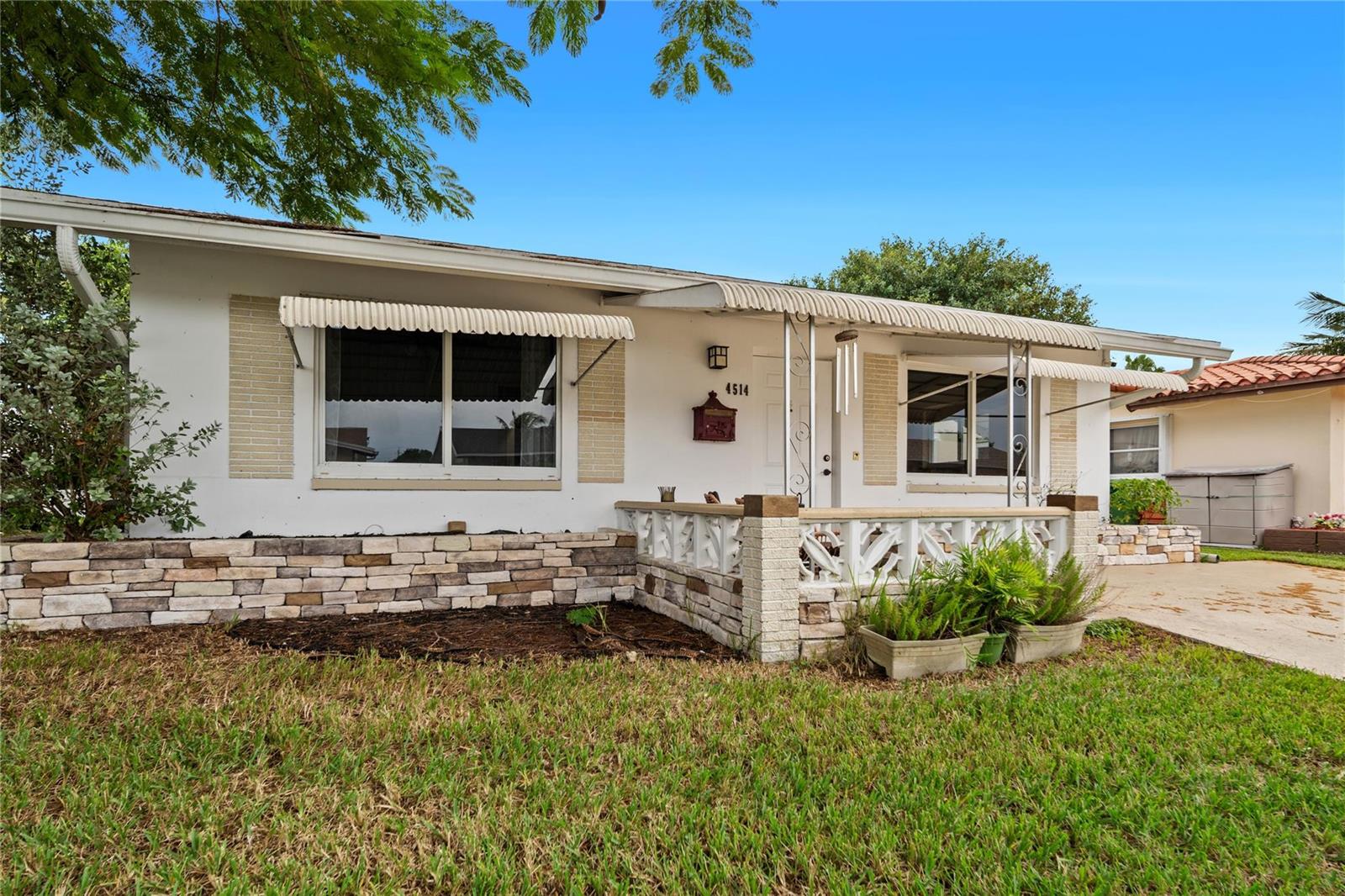 A single-story house features a stone facade, a front porch, and white metal awnings — 4514 NW 49th Drive, Tamarac FL 33319, TAMARAC, FL