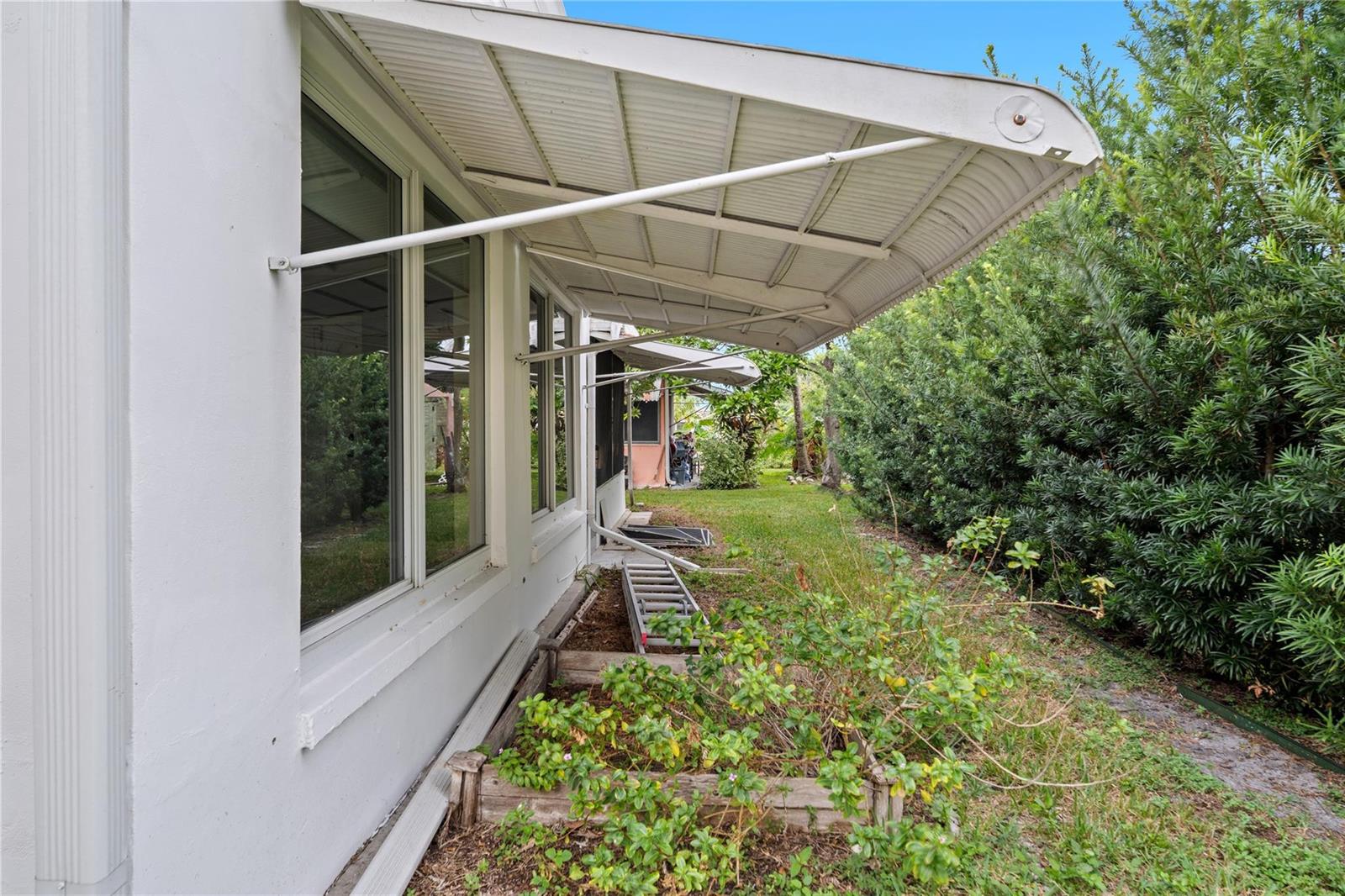 A white exterior wall features metal awnings over windows and a small garden bed below — 4514 NW 49th Drive, Tamarac FL 33319, TAMARAC, FL