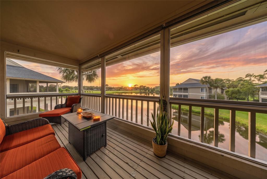 A screened-in balcony with outdoor furniture overlooks a lake at sunset — 11 MAGNOLIA DRIVE S UNIT 11, ORMOND BEACH, FL