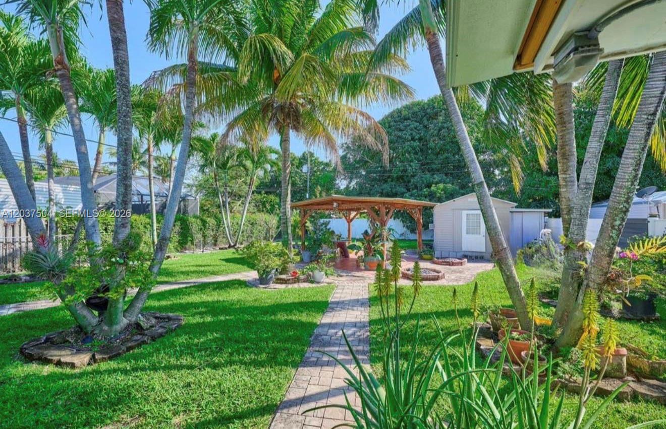 A backyard features a brick walkway leading to a wooden gazebo and a storage shed — 612 W Drew St, Lantana FL 33462, LANTANA, FL