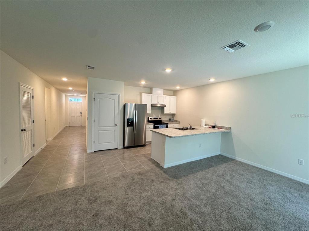 An open-concept kitchen with stainless steel appliances and a breakfast bar overlooks a carpeted area — 603 MUSKRAT DRIVE, KISSIMMEE, FL