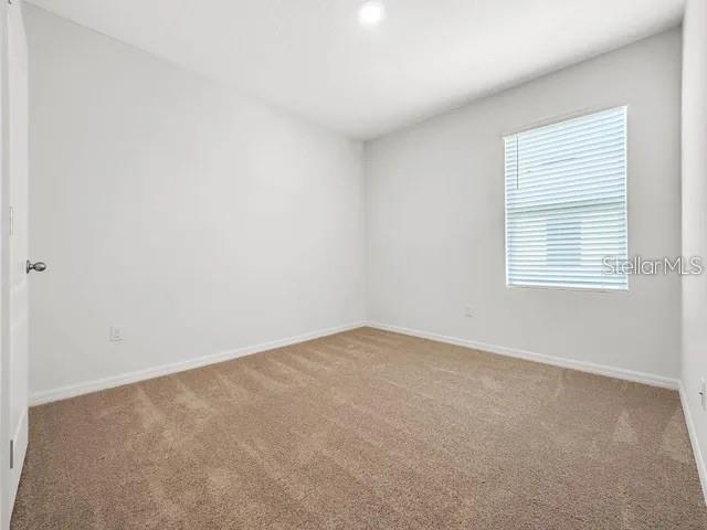 An empty bedroom features light gray walls, beige carpeting, and a window with blinds — 603 MUSKRAT DRIVE, KISSIMMEE, FL