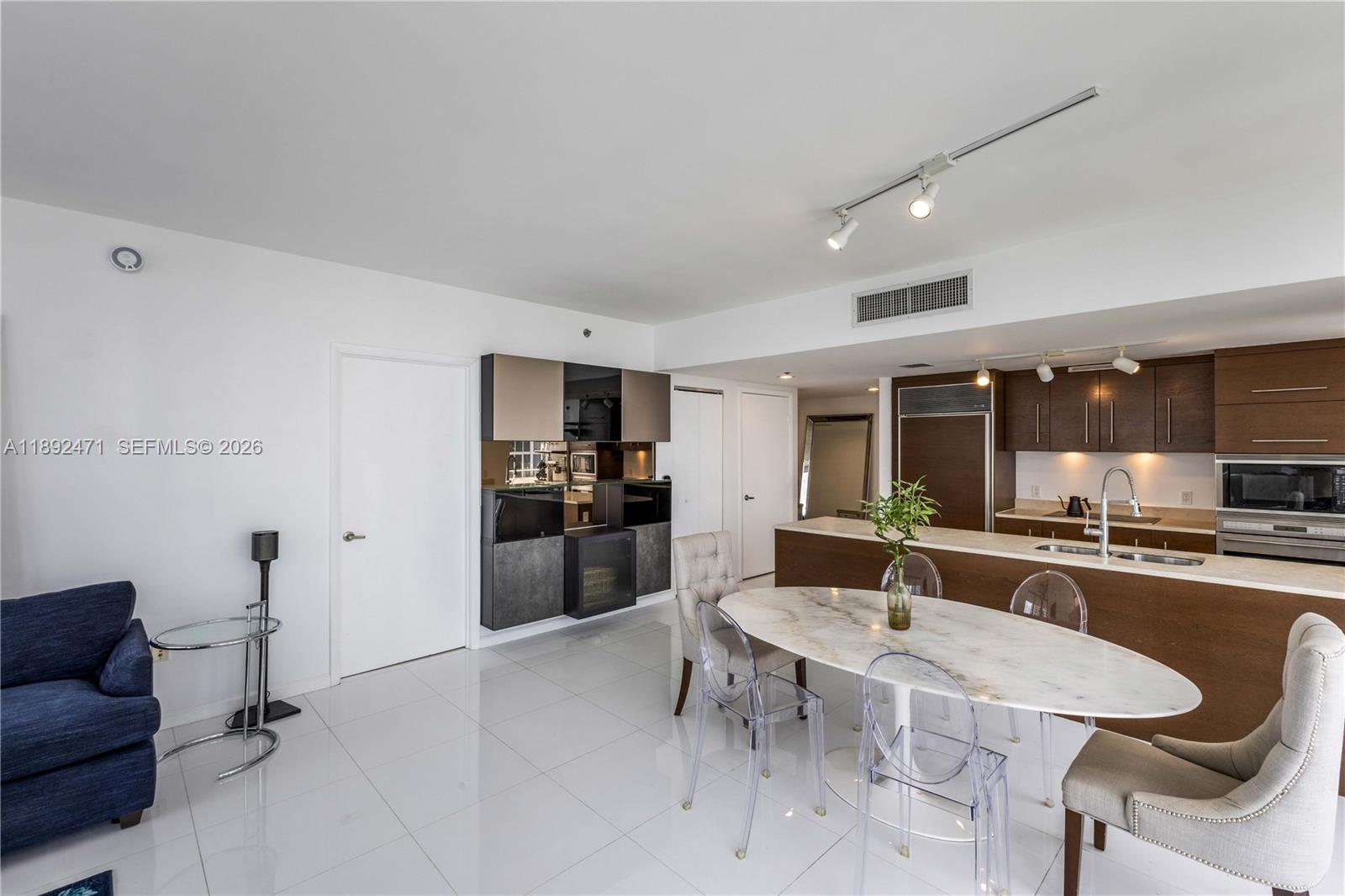A modern kitchen and dining area feature white tile floors, marble table, and dark cabinetry — 475 Brickell Ave # 4015, Miami FL 33131, MIAMI, FL