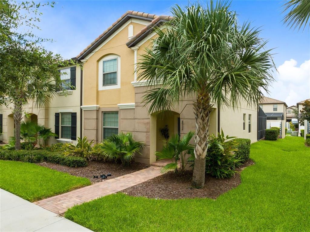 A two-story tan stucco townhouse with a palm tree and a brick walkway in front — 8932 ADRIATICO LANE, KISSIMMEE, FL