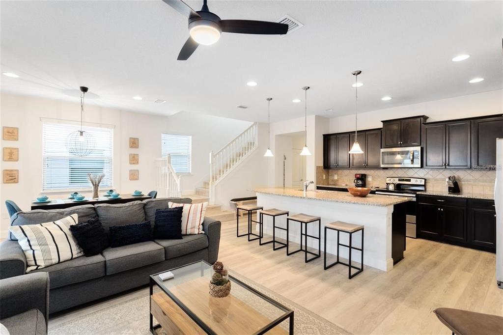 An open-concept living room and kitchen with dark cabinets, a breakfast bar, and stairs — 8932 ADRIATICO LANE, KISSIMMEE, FL