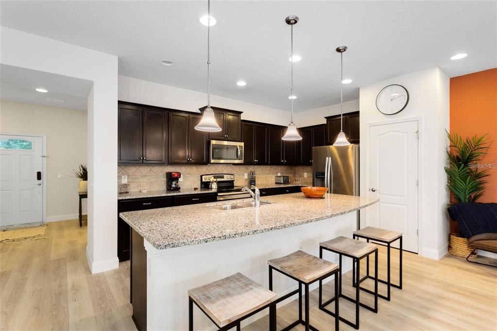 A kitchen with dark cabinets, granite countertops, a large island, and three bar stools — 8932 ADRIATICO LANE, KISSIMMEE, FL