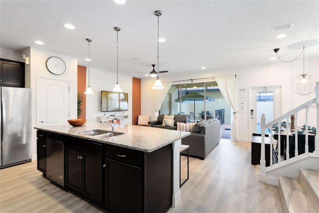 A kitchen with a dark island and granite countertops overlooks a living room and patio — 8932 ADRIATICO LANE, KISSIMMEE, FL