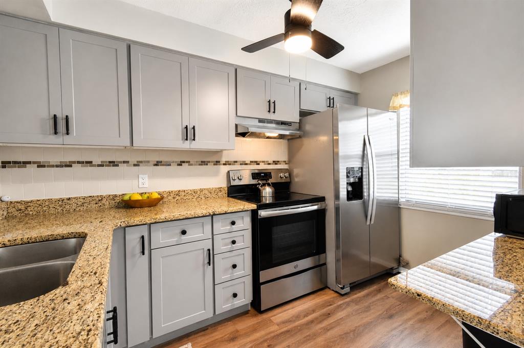 A kitchen features gray cabinets, granite countertops, stainless steel appliances, and wood-look flooring — 3683 TROPHY BOULEVARD, NEW PORT RICHEY, FL