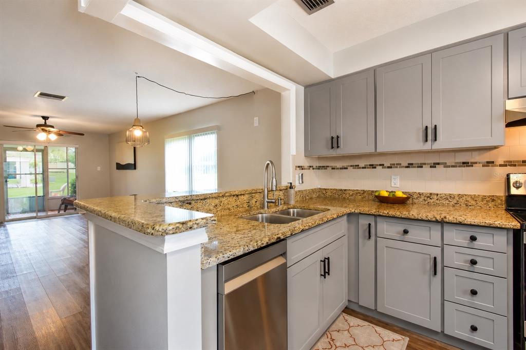 A kitchen with gray cabinets, granite countertops, and a stainless steel dishwasher overlooks a living area — 3683 TROPHY BOULEVARD, NEW PORT RICHEY, FL