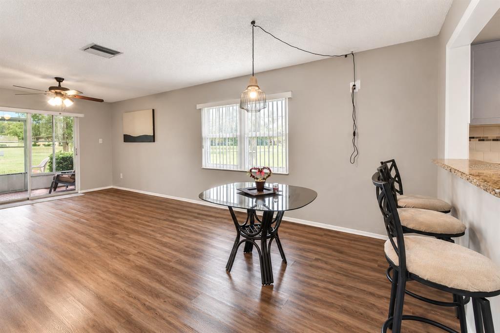 A dining area features a glass table, bar stools, wood-look flooring, and a sliding door — 3683 TROPHY BOULEVARD, NEW PORT RICHEY, FL