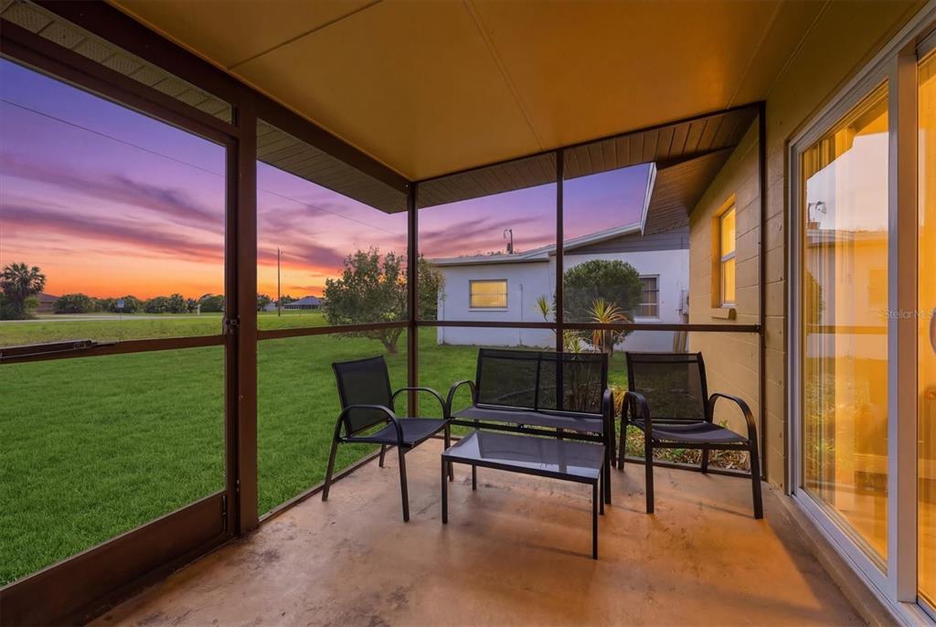 A screened-in patio features a concrete floor, outdoor furniture, and a view of a sunset — 12125 MARGARITA AVENUE, NORTH PORT, FL