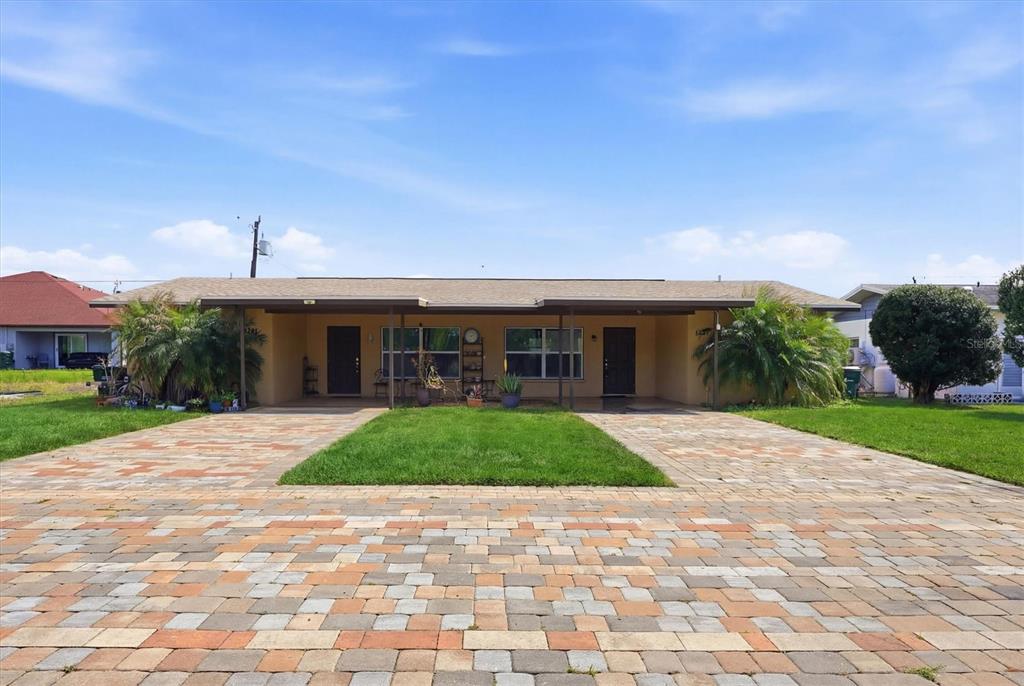 A single-story duplex features a shared covered porch and a large paver driveway — 12125 MARGARITA AVENUE, NORTH PORT, FL