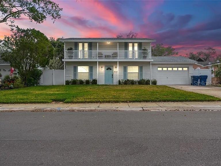 A two-story white house with a balcony, attached garage, and a front lawn at sunset — 8067 123RD STREET, SEMINOLE, FL