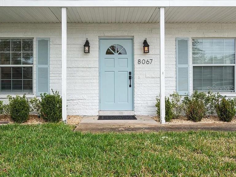 The exterior of a white brick house features a light blue front door and shutters — 8067 123RD STREET, SEMINOLE, FL