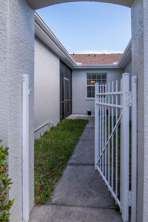 A white metal gate opens to a concrete walkway leading toward a screened-in patio area — 7308 CLEOPATRA DRIVE, LAND O LAKES, FL