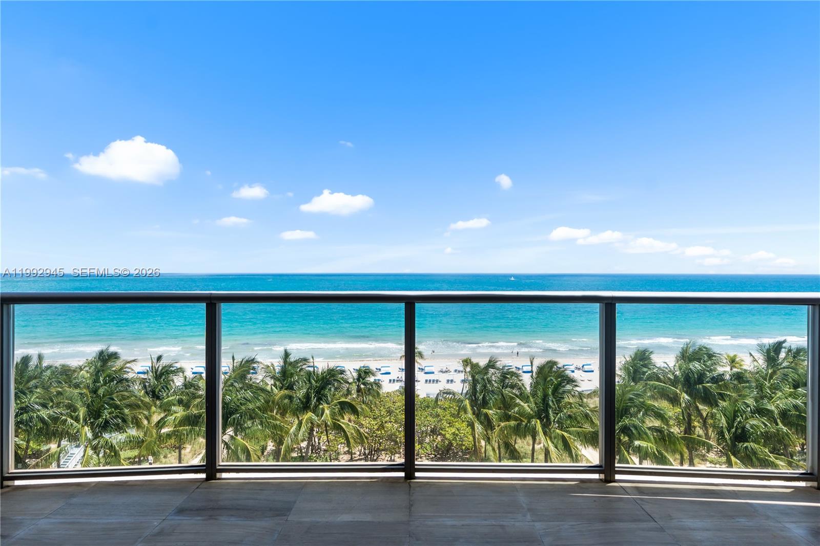 A balcony with a glass railing overlooks palm trees, a sandy beach, and the ocean — 9703 Collins Ave # 600, Bal Harbour FL 33154, BAL HARBOUR, FL