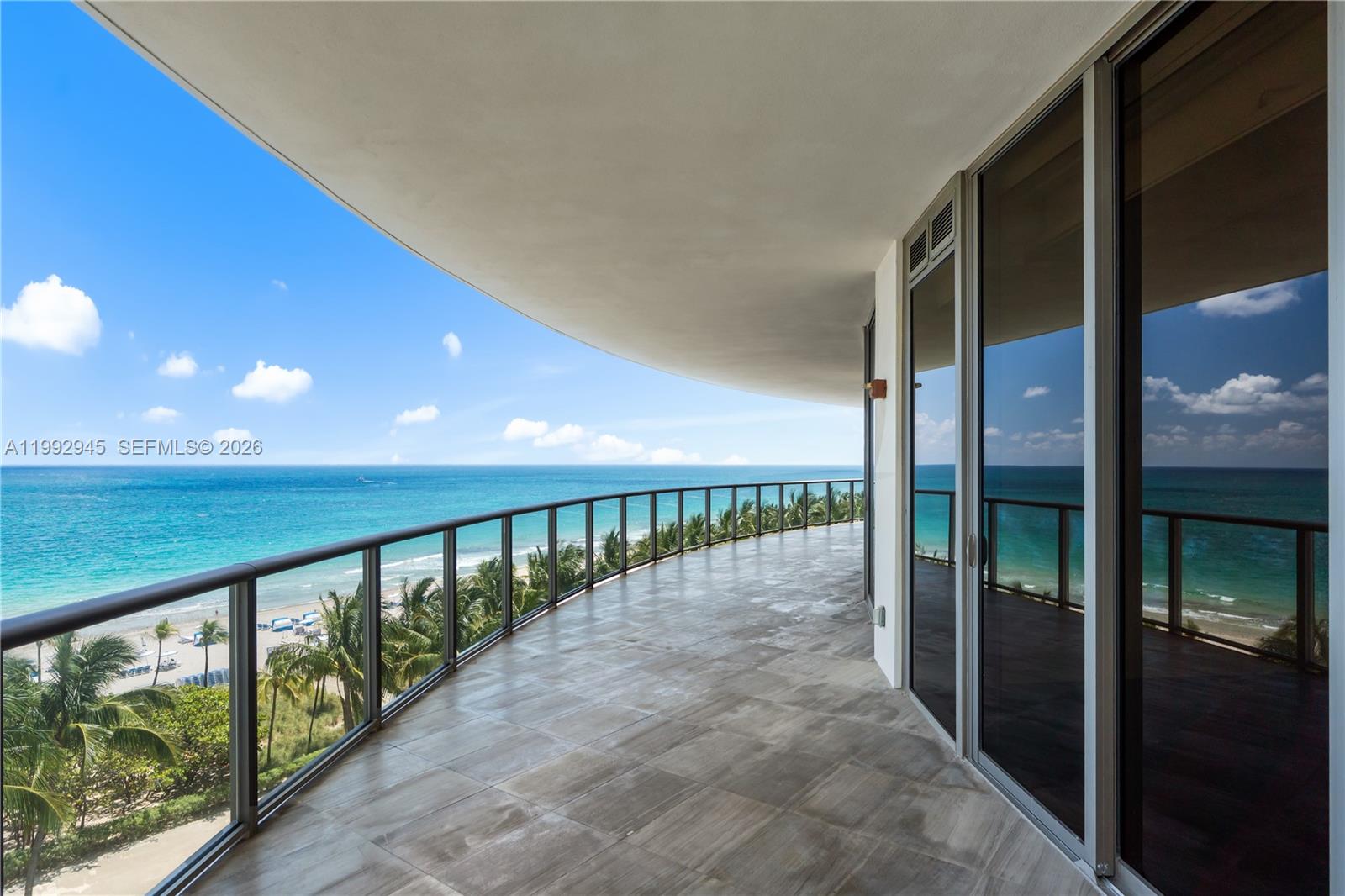 A curved balcony with tile flooring overlooks the ocean and beach through a glass railing — 9703 Collins Ave # 600, Bal Harbour FL 33154, BAL HARBOUR, FL