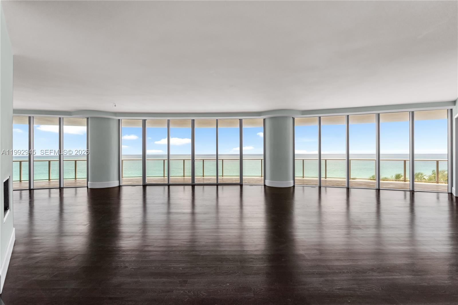 An empty room with dark wood floors features floor-to-ceiling windows overlooking the ocean — 9703 Collins Ave # 600, Bal Harbour FL 33154, BAL HARBOUR, FL