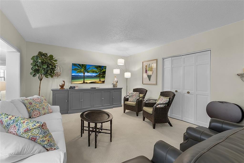A living room features a white sofa, two wicker chairs, a grey console, and carpet — INDIAN RIVER SHORES, FL