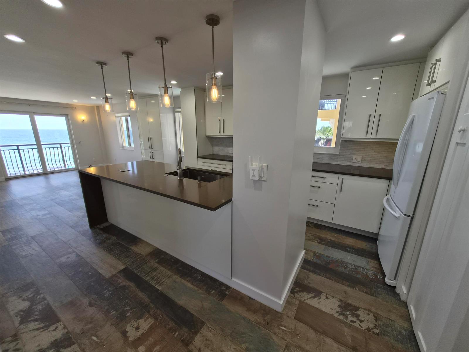 A modern kitchen features white cabinets, a dark countertop island, and ocean views through sliding doors — 1815 N Surf Road # 404, Hollywood FL 33019, HOLLYWOOD, FL