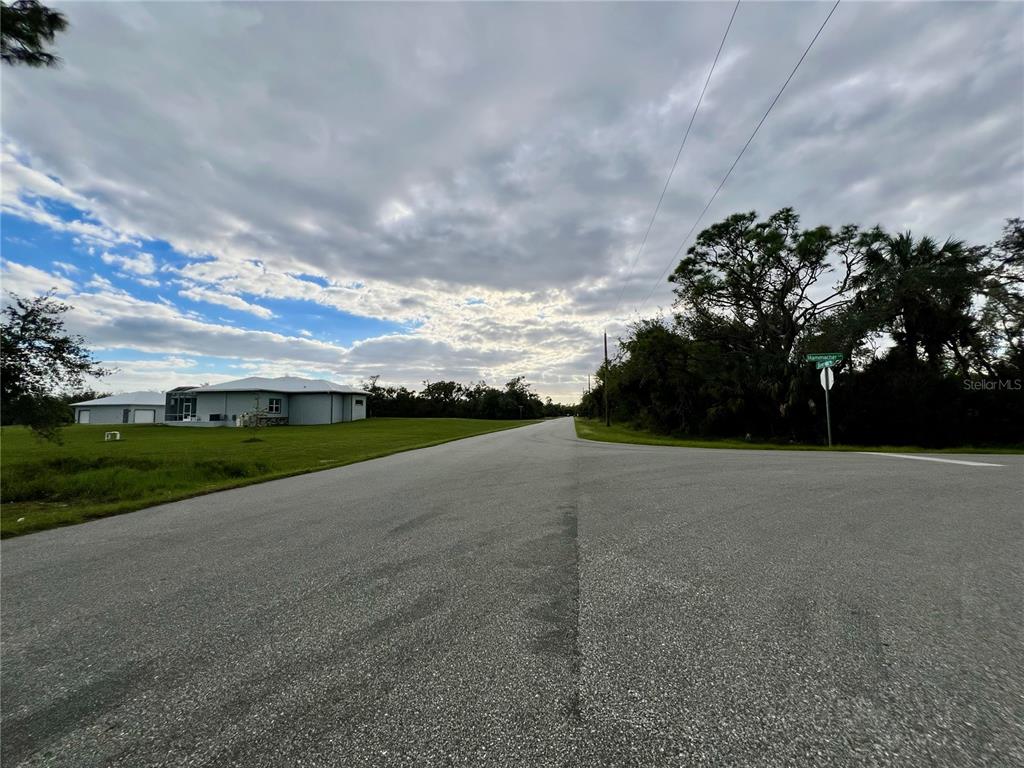 A paved road leads toward a house under a cloudy sky near a street sign — 1131 BOWMAN TERRACE, PORT CHARLOTTE, FL