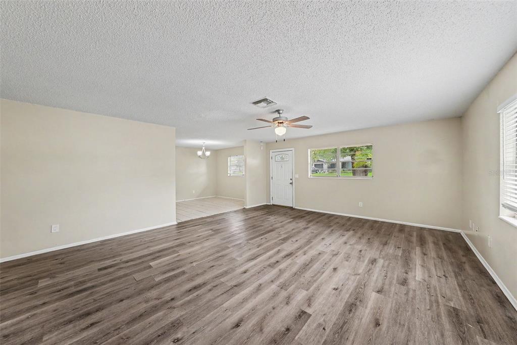 A spacious living room with light-colored walls, wood-look flooring, a ceiling fan, and an entryway — 2451 GLENVIEW DRIVE, LAND O LAKES, FL