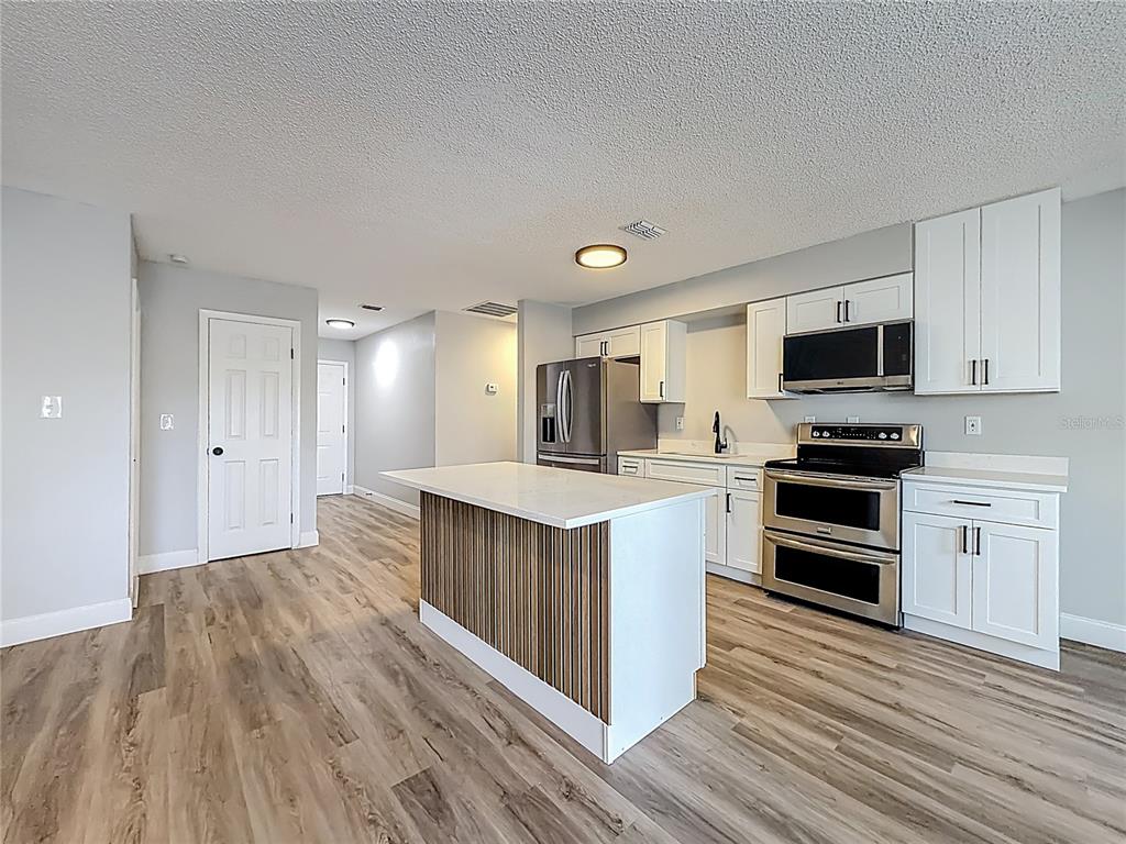 A kitchen features white cabinets, stainless steel appliances, a wood-paneled island, and wood-look flooring — 8940 SE 88TH STREET, OCALA, FL