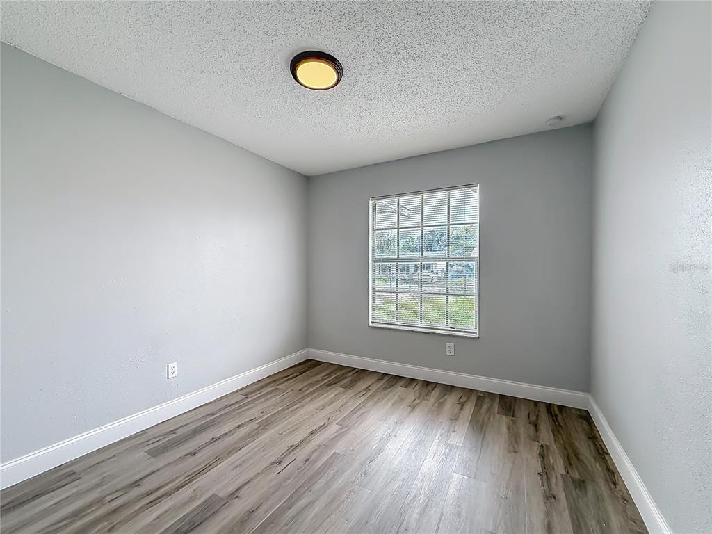 An empty bedroom features light gray walls, wood-look flooring, and a central ceiling light fixture — 8940 SE 88TH STREET, OCALA, FL