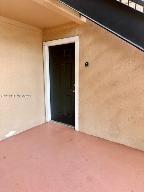 A black front door to a residential unit is set into a tan stucco wall — 10670 SW 156th Pl # 301, Miami FL 33196, MIAMI, FL