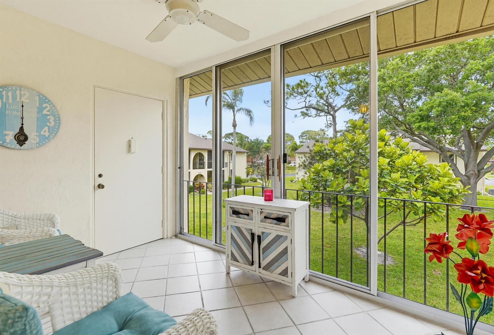 A sunroom features white tile flooring, wicker furniture, a small cabinet, and sliding glass doors — 119 Lake Pine Circle # 2, FL 33463, FL