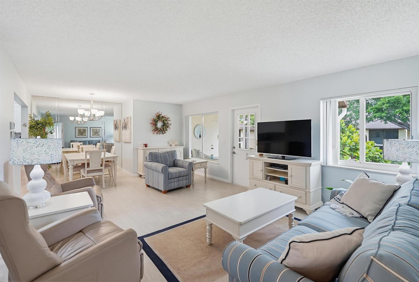 A bright living room features light wood flooring, a striped sofa, and a dining area — 119 Lake Pine Circle # 2, FL 33463, FL