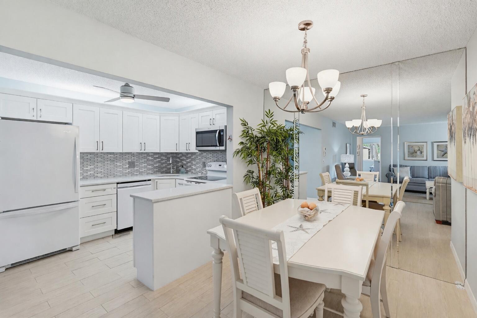 A white kitchen with a breakfast bar opens to a dining area with a chandelier — 119 Lake Pine Circle # 2, FL 33463, FL
