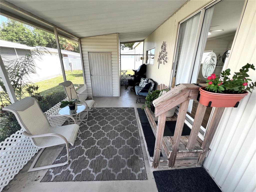 A screened-in porch features a patterned area rug, patio furniture, and wooden steps — 5316 53RD AVENUE E UNIT R36, BRADENTON, FL