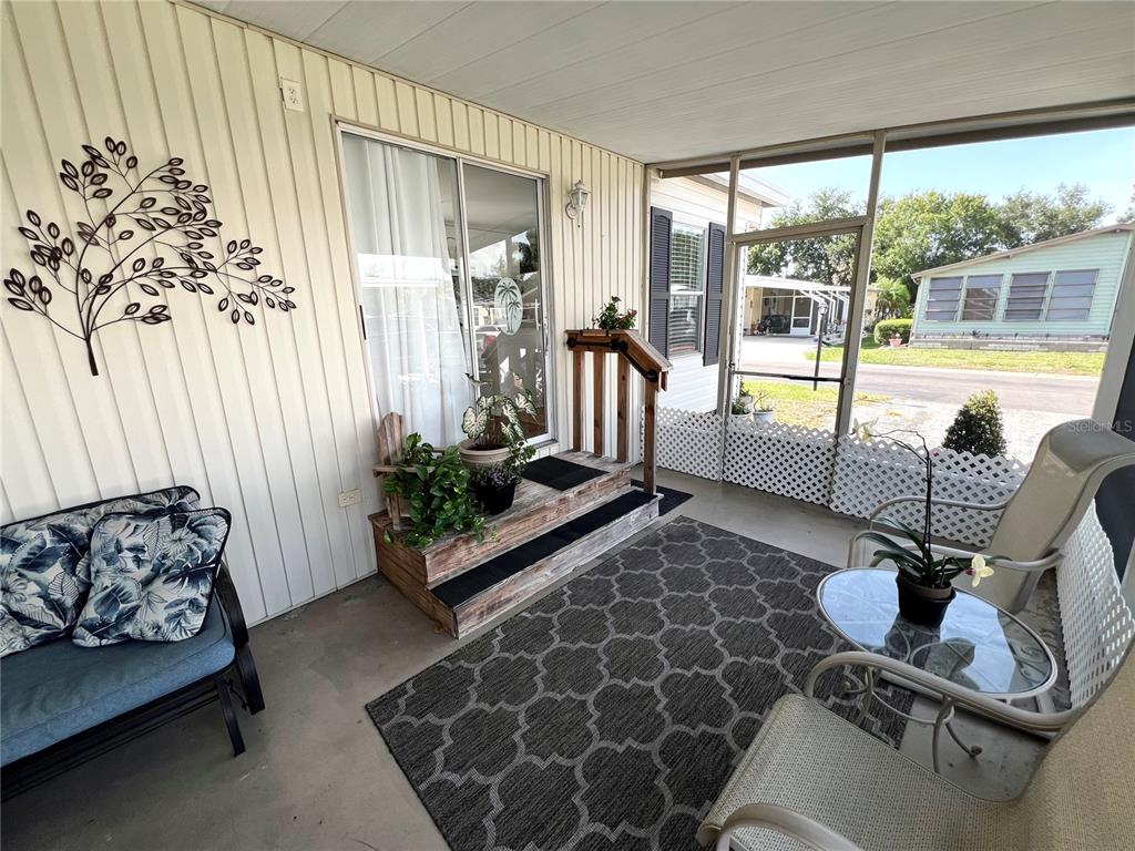 A screened-in porch features a patterned rug, patio furniture, and steps leading to a sliding door — 5316 53RD AVENUE E UNIT R36, BRADENTON, FL