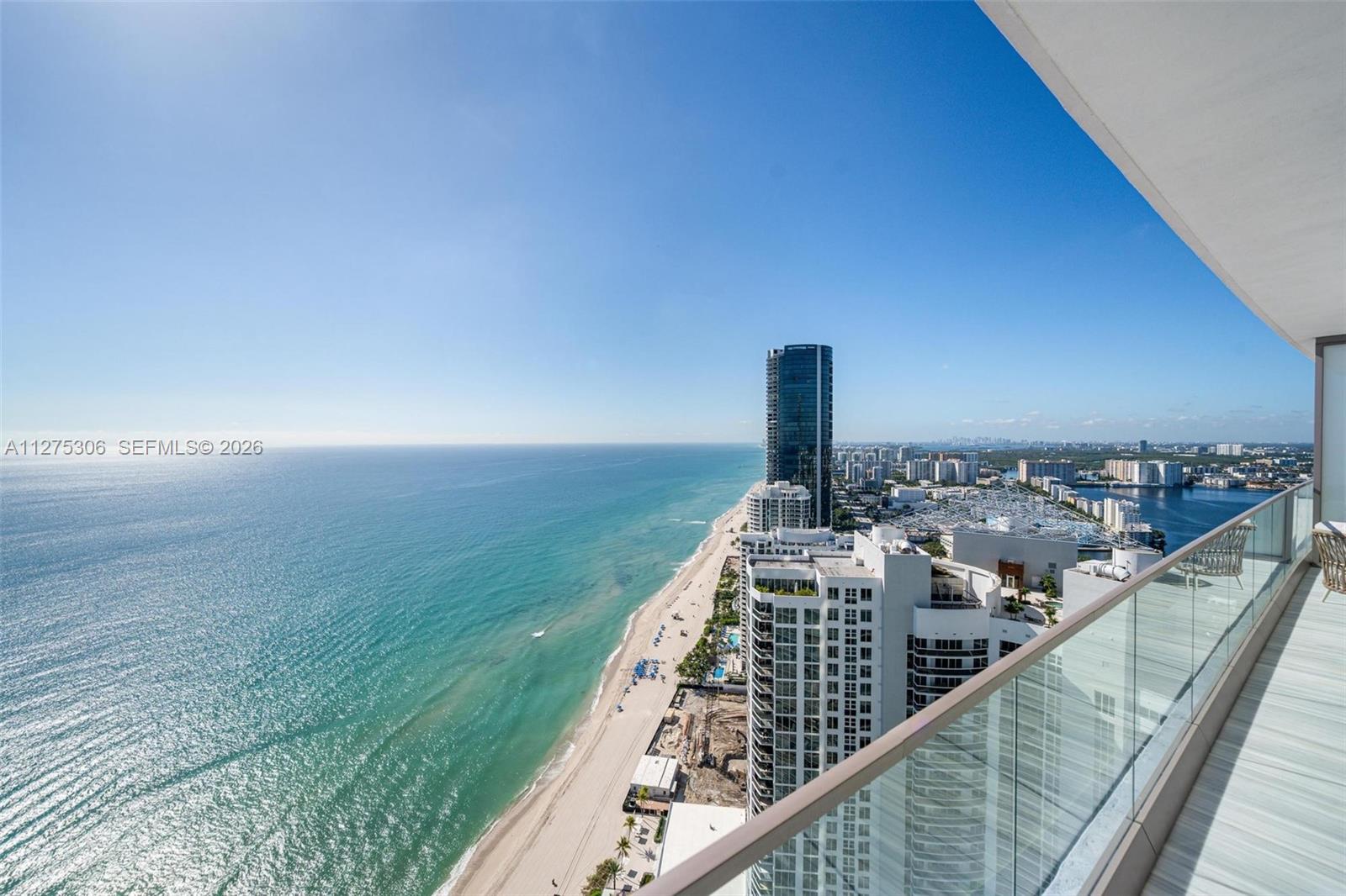 A high-rise balcony overlooks a sandy beach, the ocean, and surrounding coastal buildings — 18975 E Collins Ave # 3802, Sunny Isles Beach FL 33160, SUNNY ISLES BEACH, FL