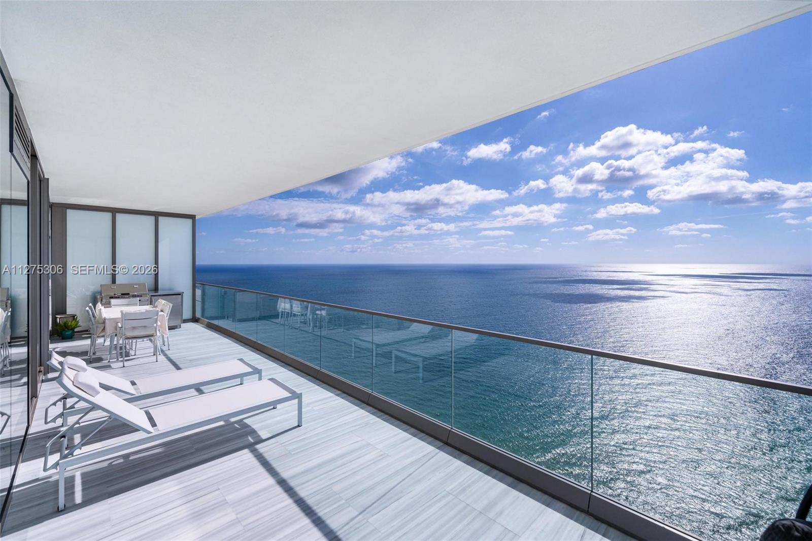 A balcony with lounge chairs and a dining set overlooks the ocean — 18975 E Collins Ave # 3802, Sunny Isles Beach FL 33160, SUNNY ISLES BEACH, FL