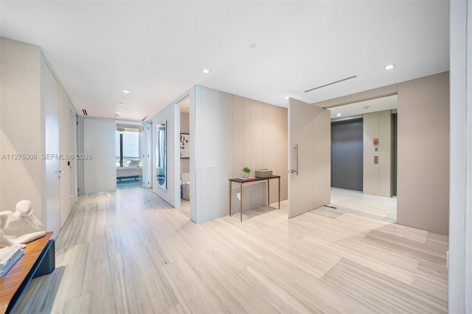A modern entryway features light wood-look tile flooring, a pivot door, and a console table — 18975 E Collins Ave # 3802, Sunny Isles Beach FL 33160, SUNNY ISLES BEACH, FL