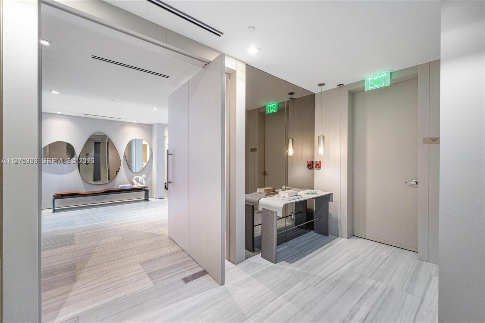 A modern hallway features light wood-look flooring, a mirrored wall, and a minimalist console table — 18975 E Collins Ave # 3802, Sunny Isles Beach FL 33160, SUNNY ISLES BEACH, FL