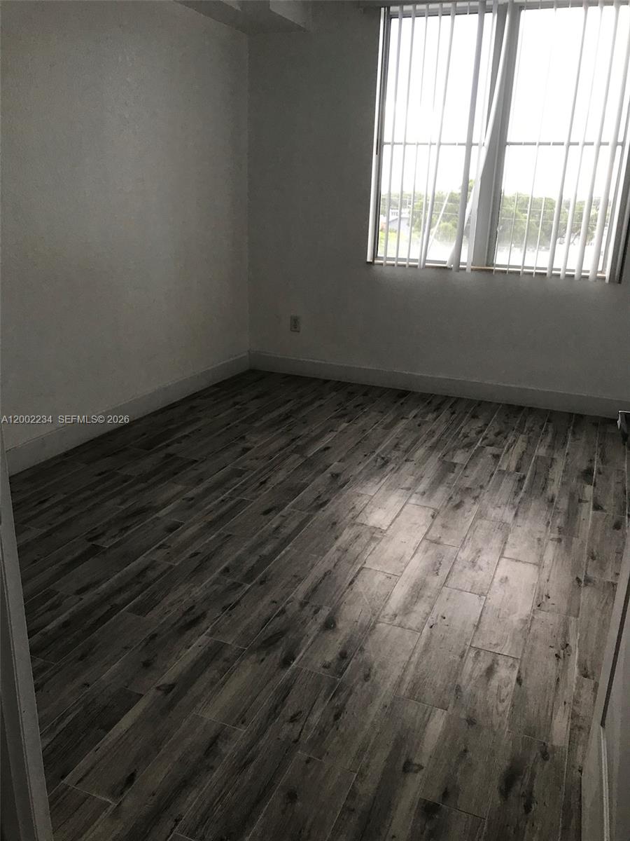 An empty room features gray wood-look tile flooring and a window with vertical blinds — 1830 Radius Dr # 407, Hollywood FL 33020, HOLLYWOOD, FL