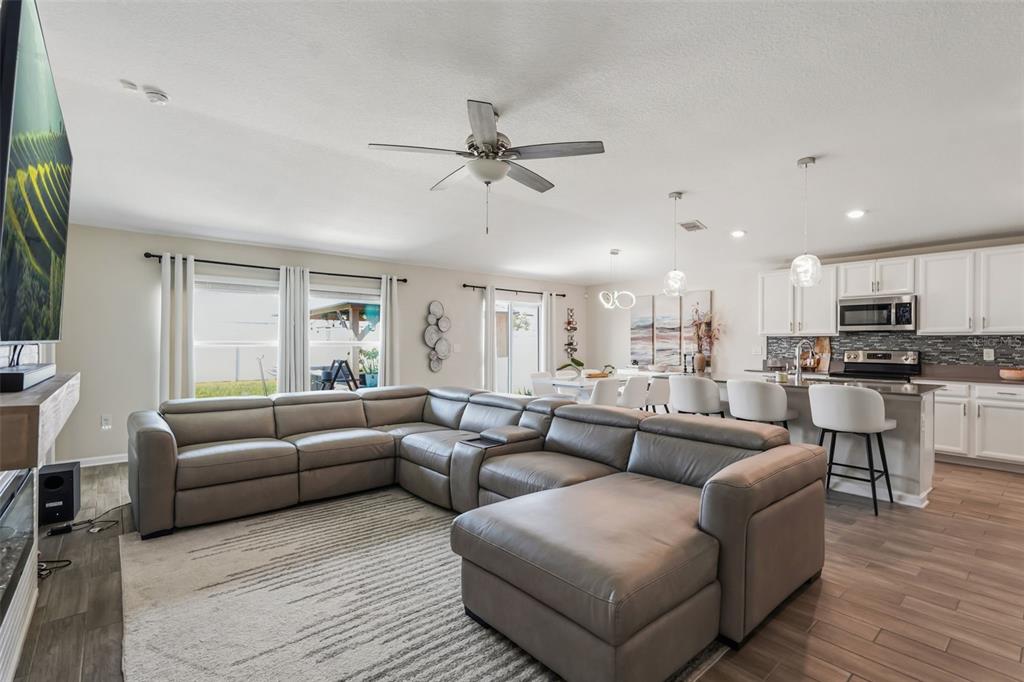 A spacious open-concept living room features a large gray sectional sofa and a modern kitchen — 4230 HOLSTEIN STREET, ST CLOUD, FL