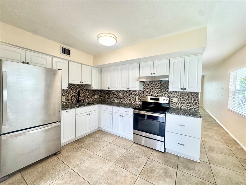 A kitchen features white cabinets, stainless steel appliances, a mosaic backsplash, and tiled flooring — 2020 WORLD PARKWAY BOULEVARD UNIT 54, CLEARWATER, FL