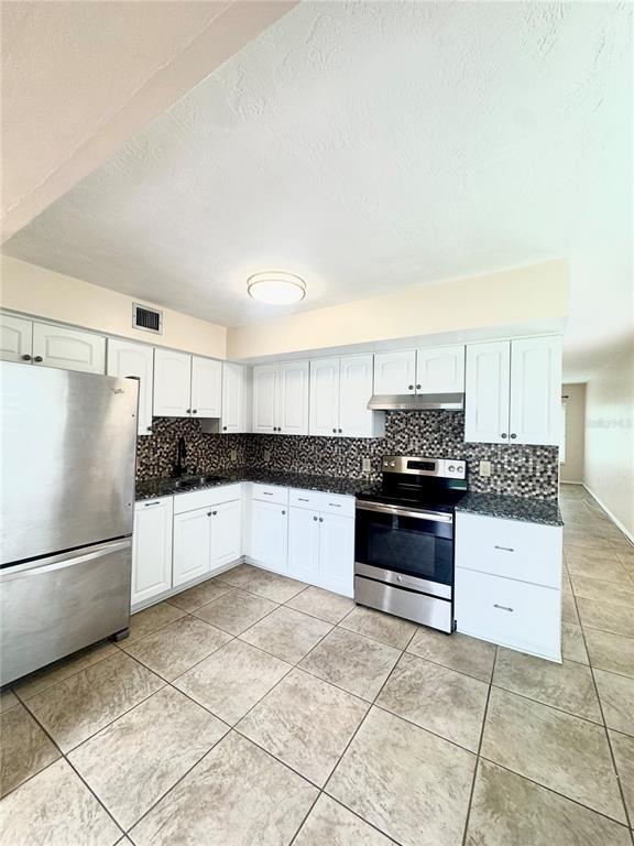 A kitchen features white cabinets, stainless steel appliances, a mosaic backsplash, and tiled flooring — 2020 WORLD PARKWAY BOULEVARD UNIT 54, CLEARWATER, FL